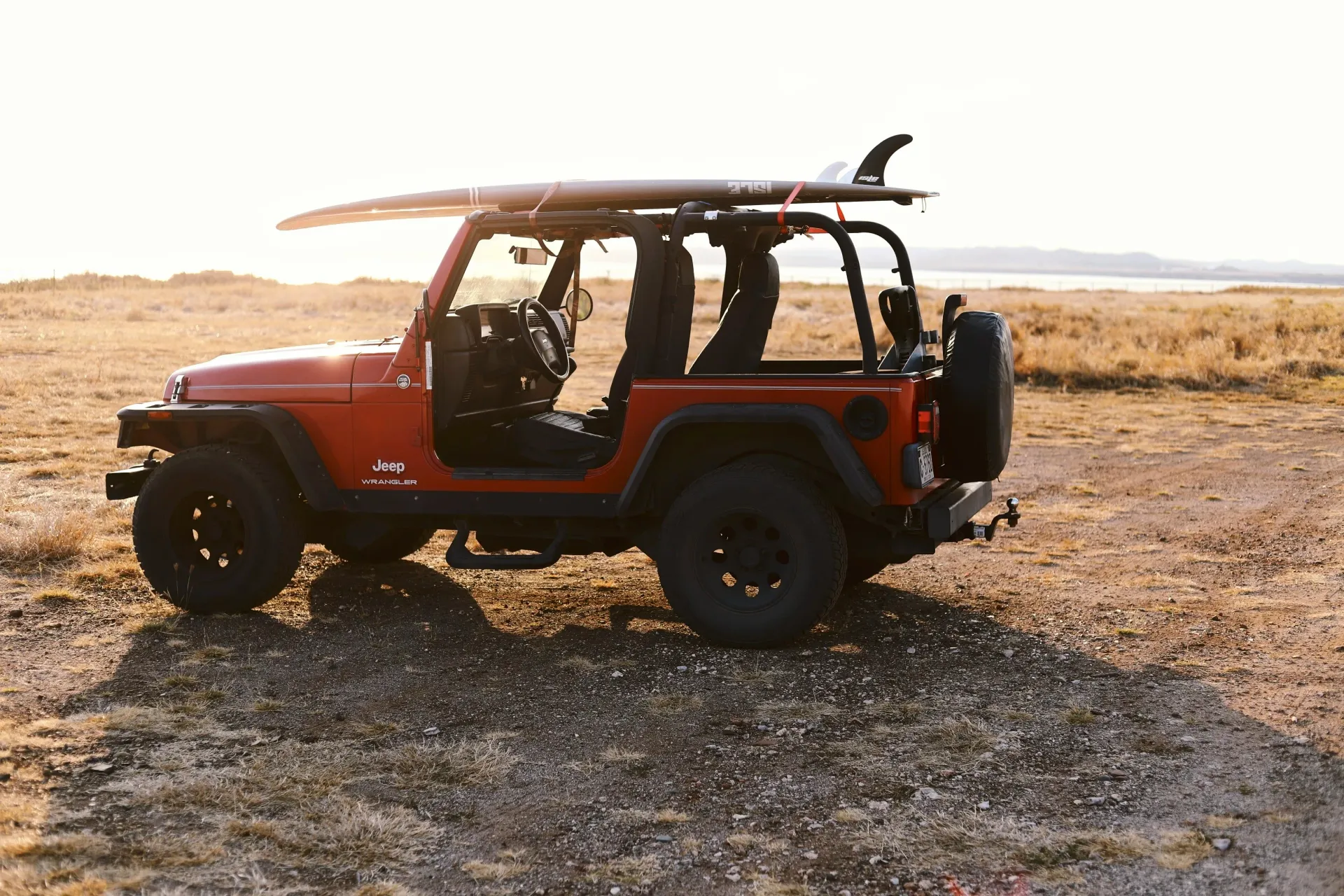 A red Jeep with a surfboard at golden hour