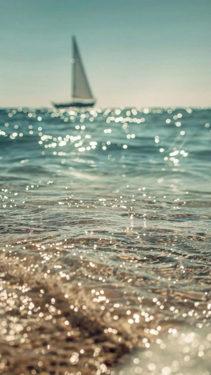 Sunlit ocean water with a sailboat on the horizon