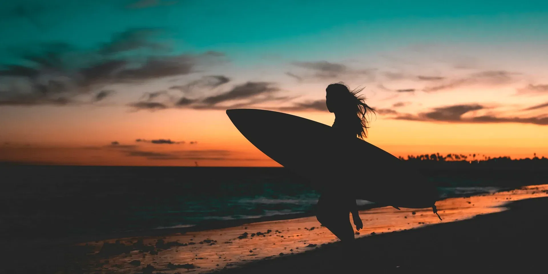A surfer silhouetted against a coastal sunset